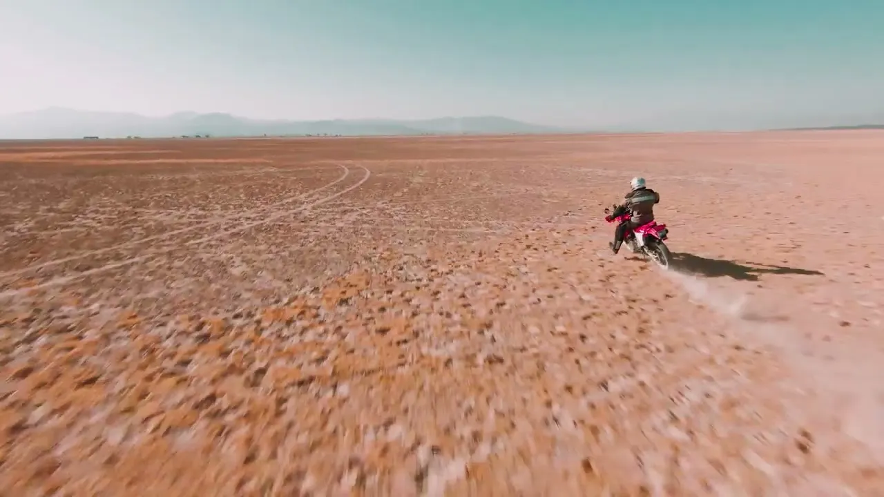 Moto cruzando un desierto visto desde arriba, con la estela de polvo